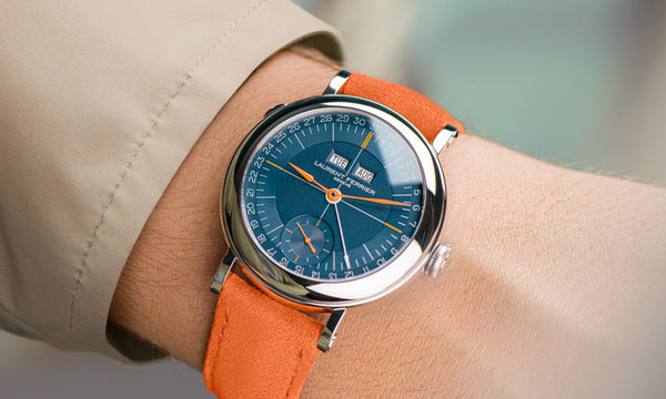 Classic "École Annual Calendar" blue navy and orange stainless steel watch by Swiss award winning fine watchmaker Laurent Ferrier on man's wrist with beige jacket sleeve showing