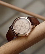 Classic Origin Beige by renowned watchmaker Laurent Ferrier laying on its side on a tan colored wooden stick. Photo Antoine Martin
