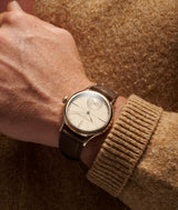 Classic Origin "Beige" on white man wrist against caramel wool sweater background with reflections on watch's sapphire front dial glass.