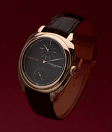 crown-side profile of laurent ferrier square regulateur watch with black dial and red-gold case on brown alligator bracelet on deep red gradient background