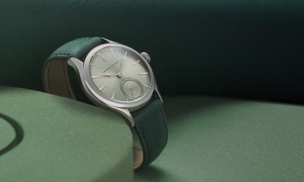Lifestyle front view of Laurent Ferrier fine watchmaker's Classic Micro-Rotor with "Magnetic Green" reflective dial and forest green bracelet. The watch is resting on a green circle of hard foam against a deep green background.