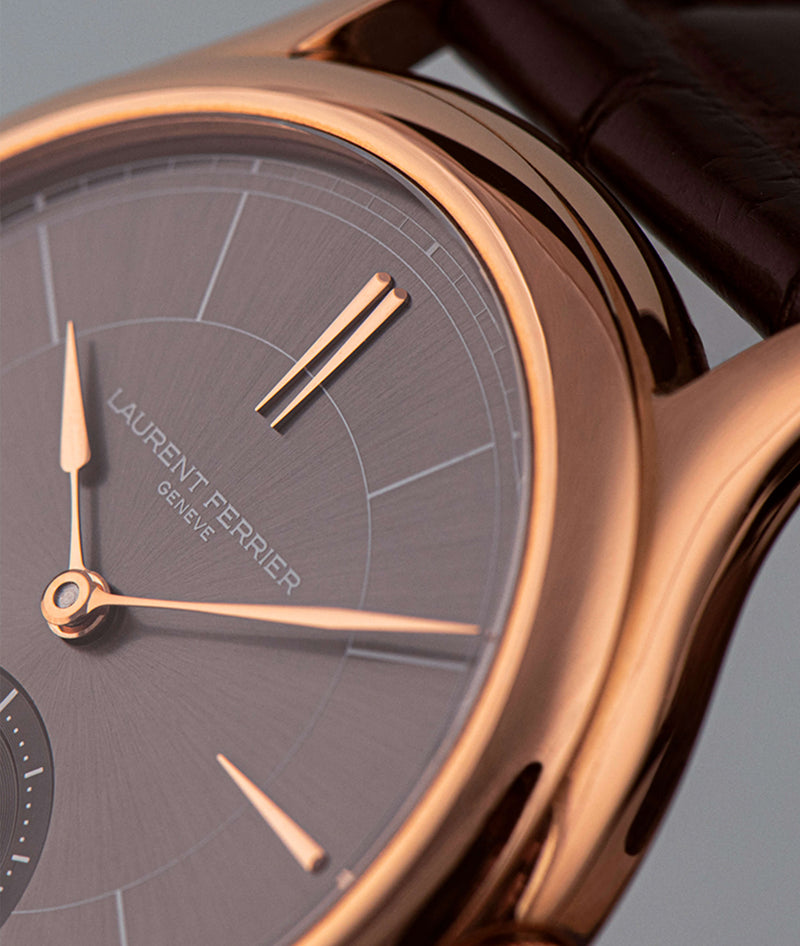 closeup of laurent ferrier classic micro rotor watch in red-gold case and assegai hands and indexes on grey sunburst dial with brown crocodile bracelet on light blue background