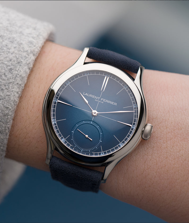 Classic Origin "Blue" on white woman female wrist against blurry blue background with reflections on watch's sapphire front dial glass.