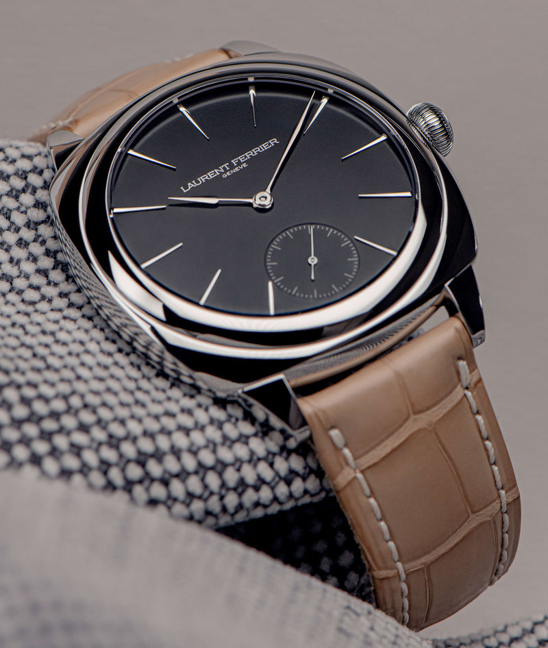 Laurent Ferrier square cushion shaped watch in stainless steel with light beige tan alligator bracelet with black opaline dial resting on black and white textures fabric