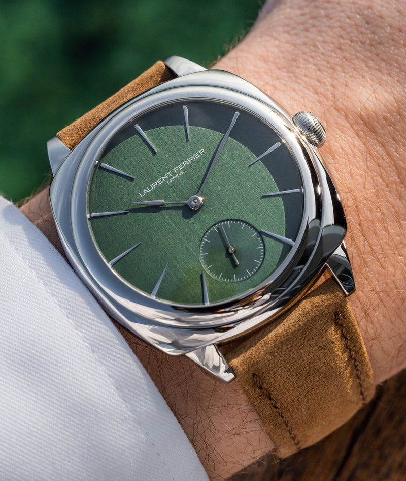 The new stainless steel Square Micro-Rotor 'Evergreen' with lush green vertical satin finish dial and brown leather strap worn on a man's wrist in the sun against grass background.