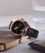 laurent ferrier square regulateur black-dial watch in red-gold case and brown alligator bracelet laying on black notebook
